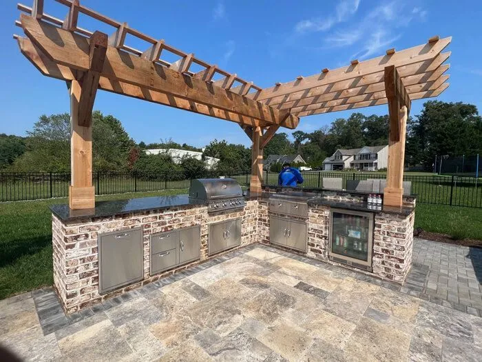L-shaped brick outdoor kitchen with a built-in grill under a cedar pergola