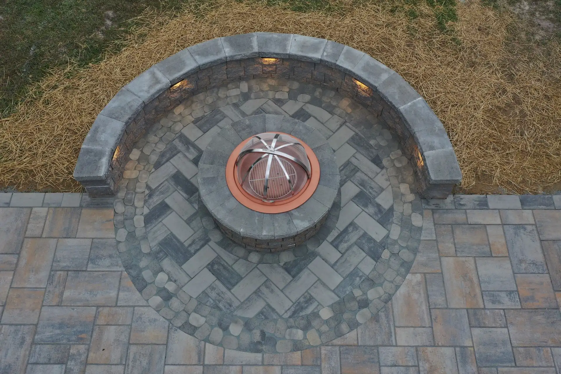 Overhead view of a circular stone patio with a fire pit, surrounded by a curved stone bench with built-in lights.