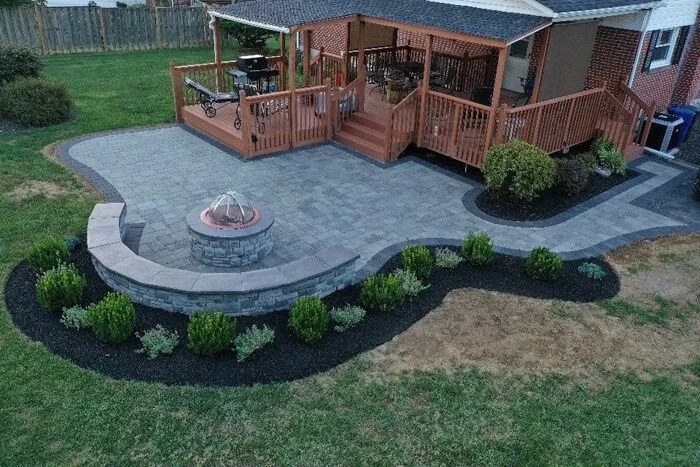 Curved paver patio with a round fire pit and stone seat wall off a wooden deck