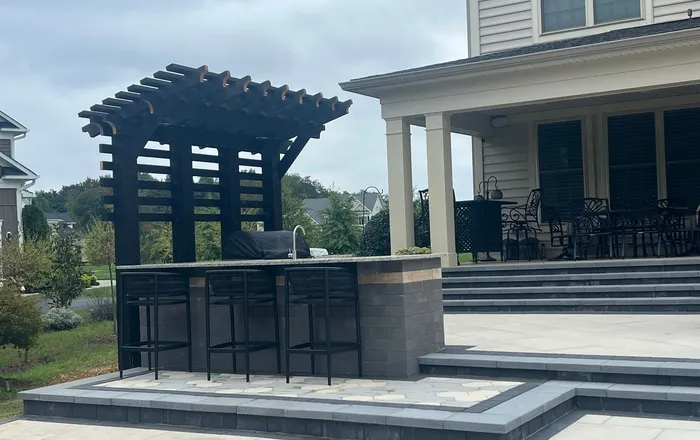 Paver patio with wide stone steps and a pergola bar beside a brick home, similar to Dundalk, MD repair work