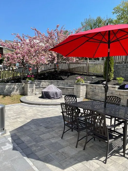 Paver patio with a dining set under a red umbrella and a raised fire pit area behind