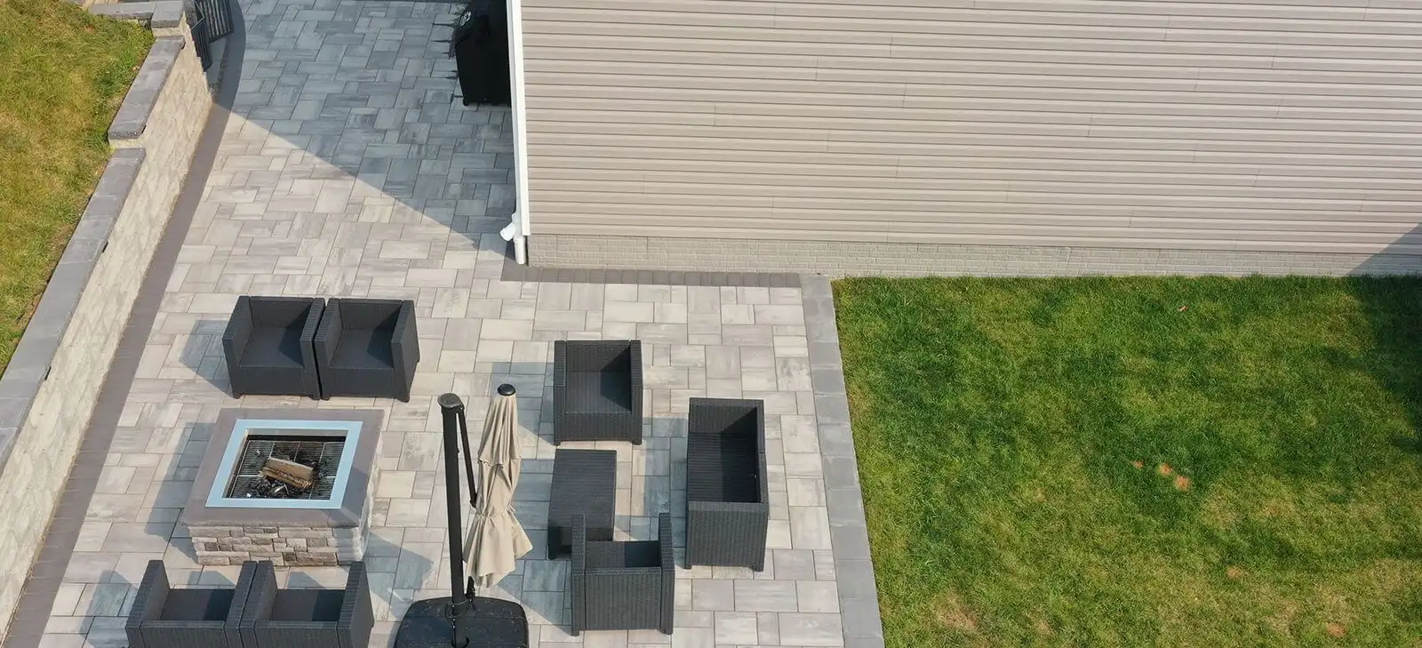 Aerial view of a paver patio with a fire table and lounge seating beside a stone retaining wall