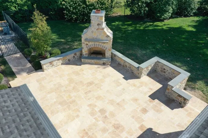 Aerial view of a tan paver patio with a stone outdoor fireplace and L-shaped seat wall