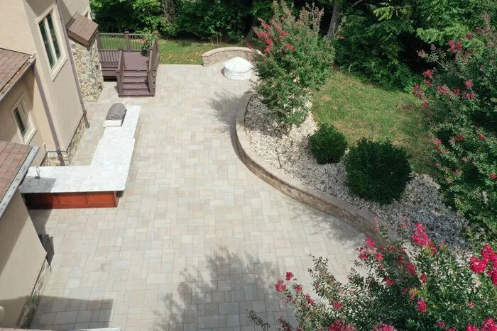 Light paver walkway along a house beside a curved garden bed with river rock edging