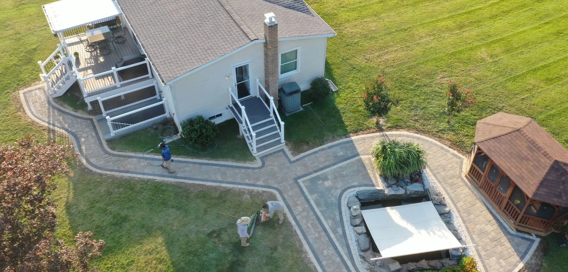 Aerial view of a paver walkway linking a home's back deck to a patio and wooden gazebo