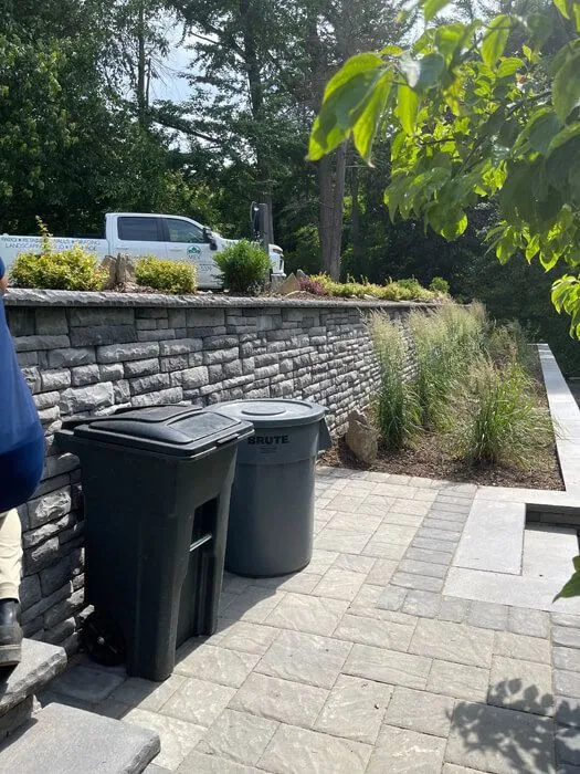 Paver side-yard walkway along a stone retaining wall with ornamental grasses