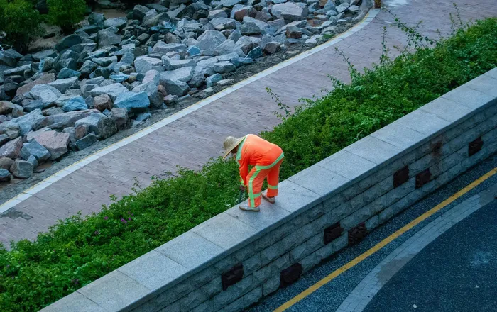 Crew member working along a granite block retaining wall beside a sloped paved path in Ellicott City, MD