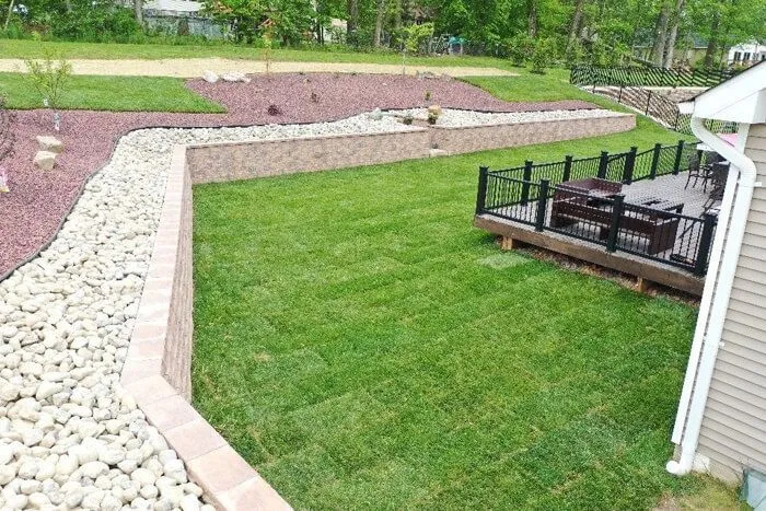 Tan block retaining wall edged with white river rock above a freshly sodded lawn
