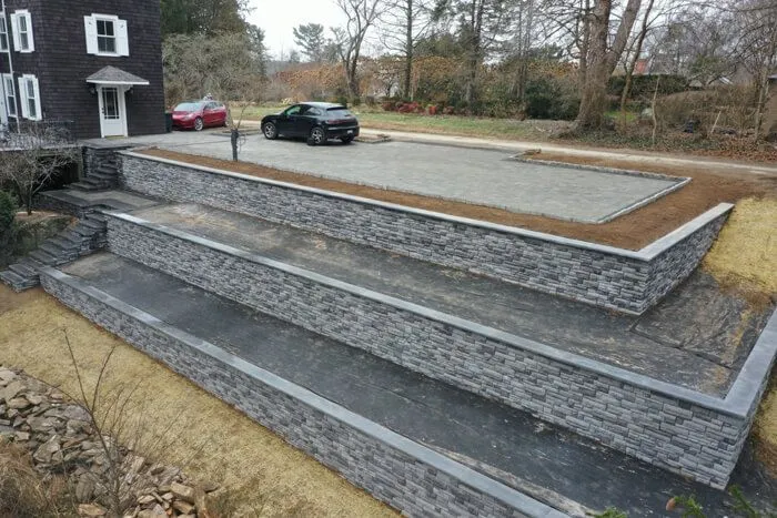 Three stacked stone retaining walls terracing a slope up to a paved parking area